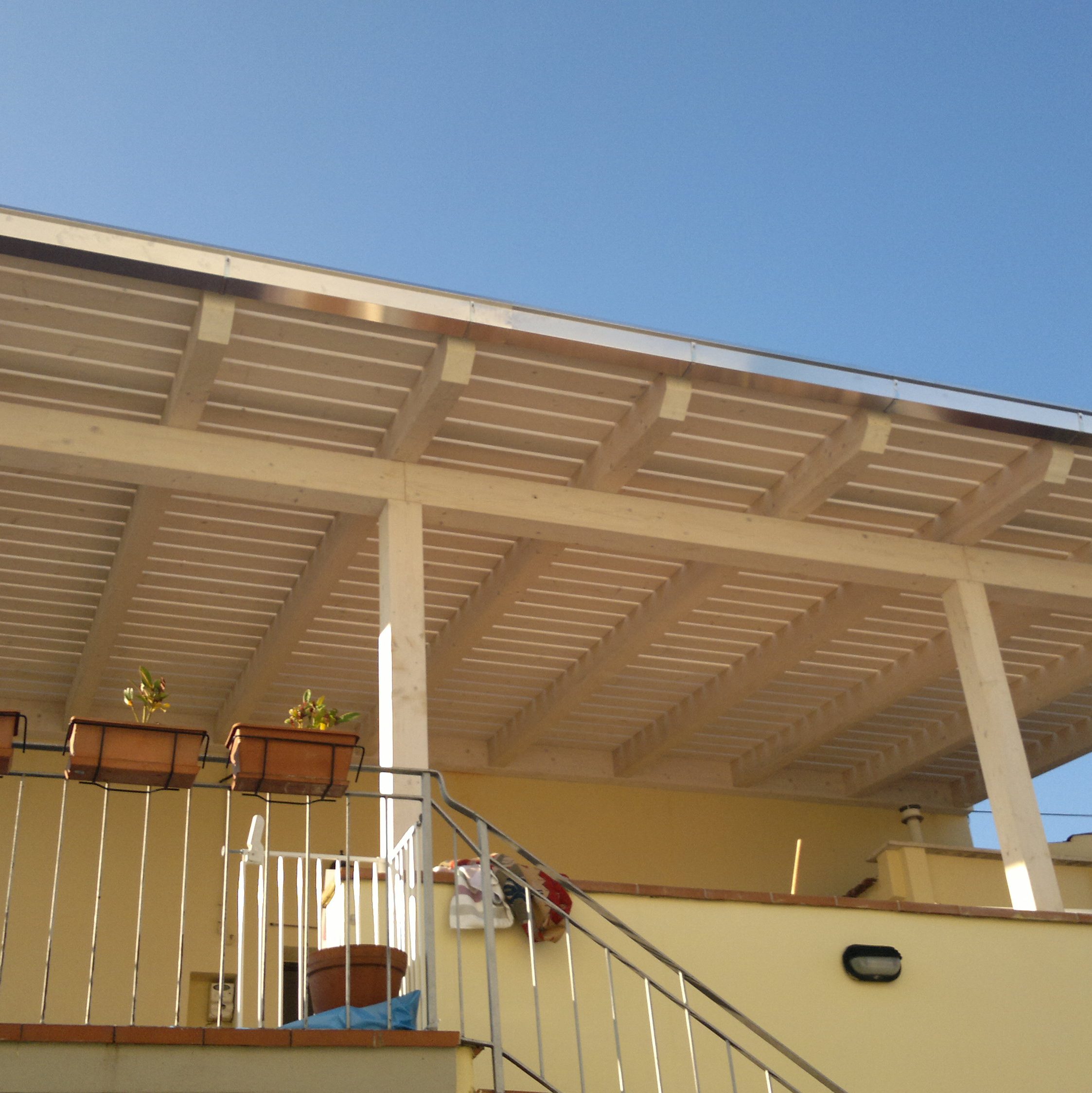 una tettoia in legno di un balconcino di una casa di clore chiaro, quasi crema