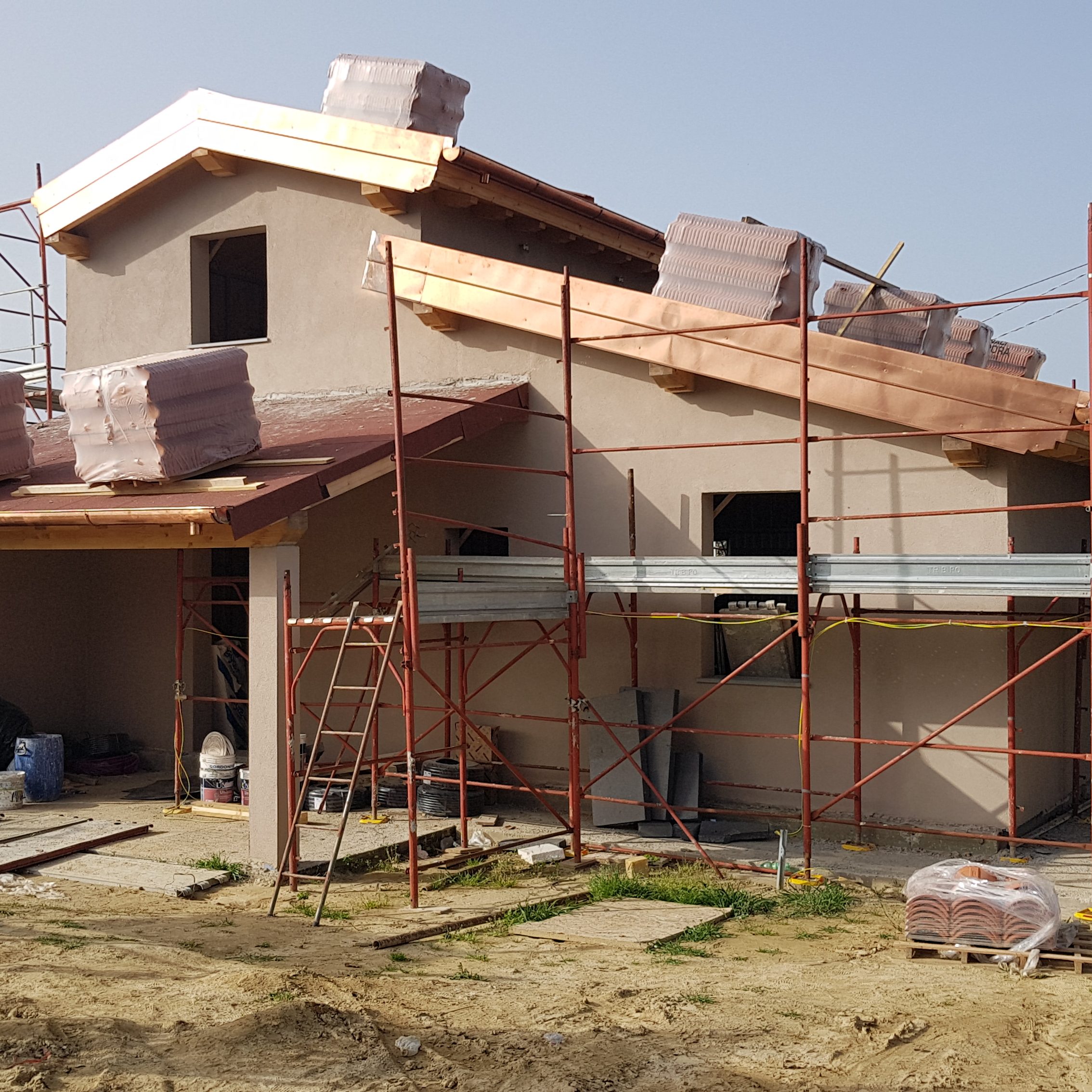 una casa in costruzione vista dall'esterno con delle impalcature intorno. sul tetto è visibile il materiale isolante ancora imballato, che andrà ad essere installato nella casa
